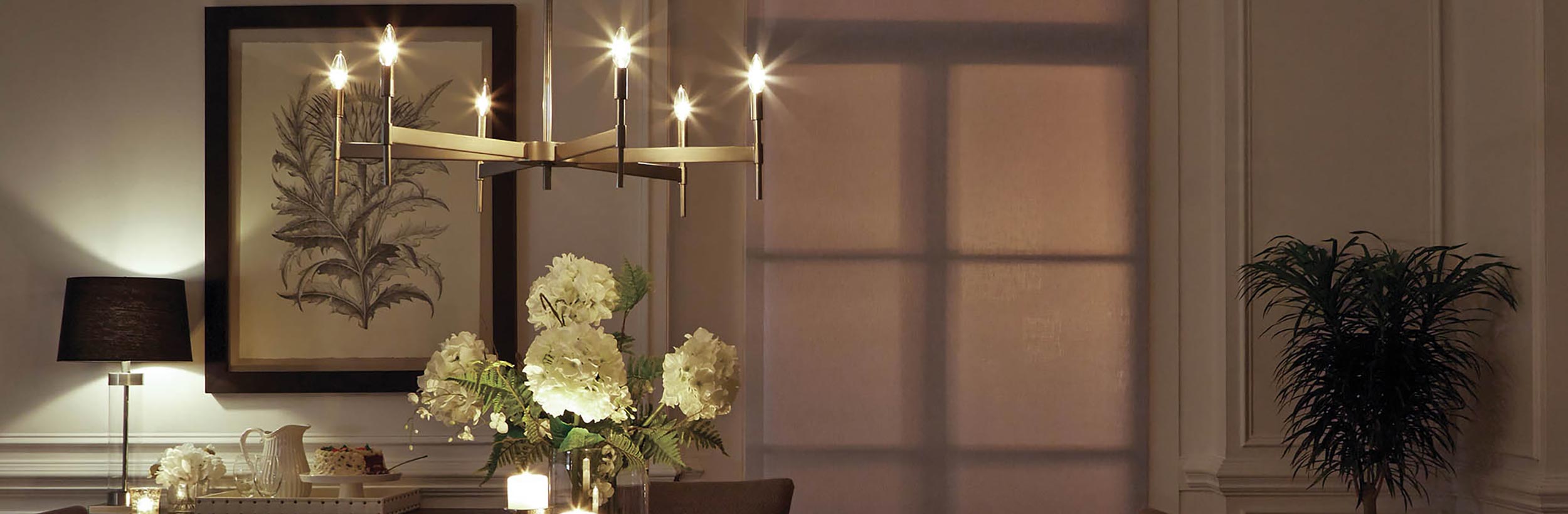 Elegant dining room with a modern chandelier, floral centerpiece, and soft lighting against a backdrop of wall art and sheer curtains.