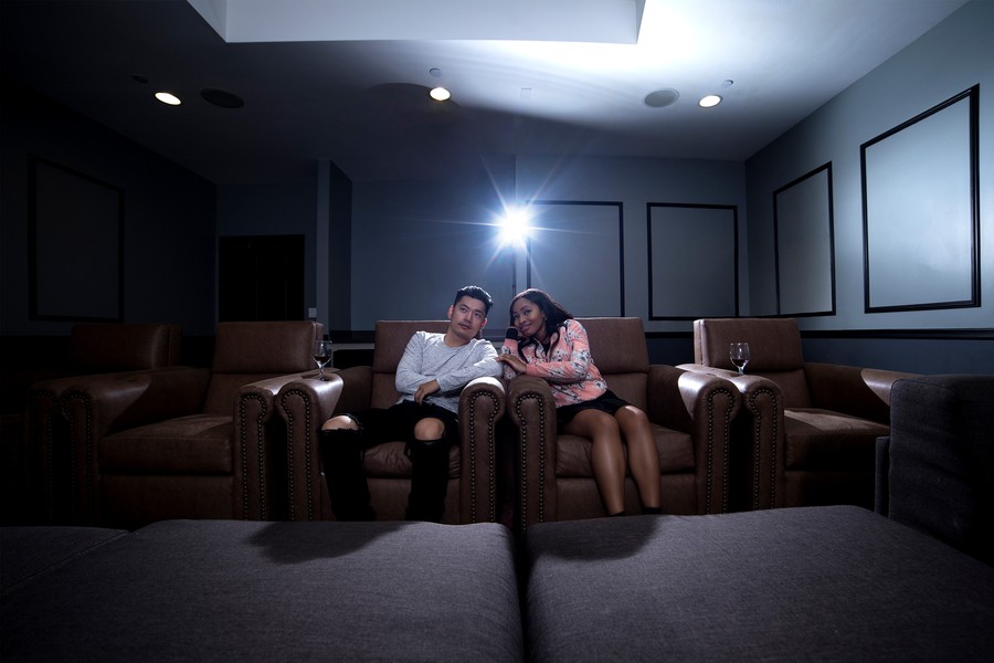 Couple sitting in brown home theater recliners with glasses of wine in the cup holders. 